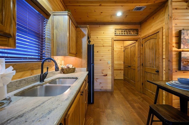 kitchen with sink, wood walls, light stone counters, wooden ceiling, and hardwood / wood-style flooring