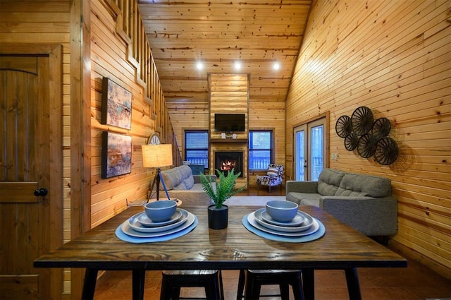 dining space with high vaulted ceiling, wooden walls, a fireplace, wooden ceiling, and french doors