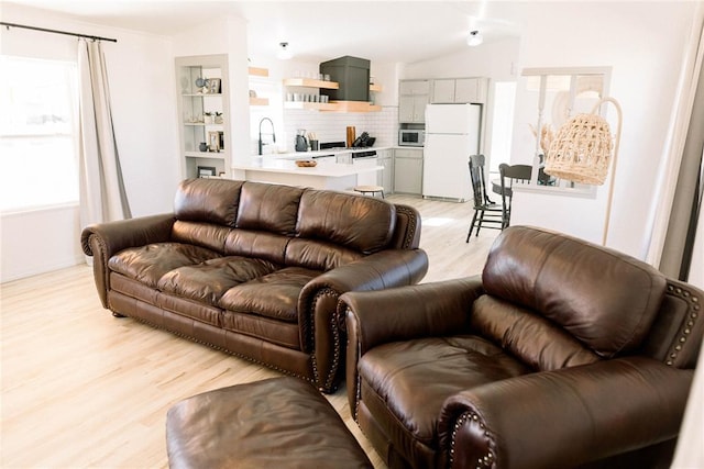 living room with lofted ceiling, sink, and light hardwood / wood-style flooring