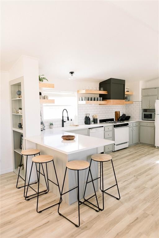 kitchen featuring sink, white appliances, a breakfast bar, decorative backsplash, and light wood-type flooring