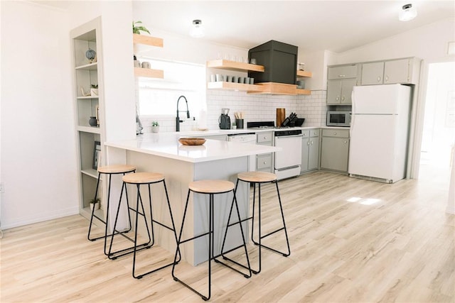 kitchen featuring a breakfast bar, tasteful backsplash, light hardwood / wood-style flooring, kitchen peninsula, and white appliances