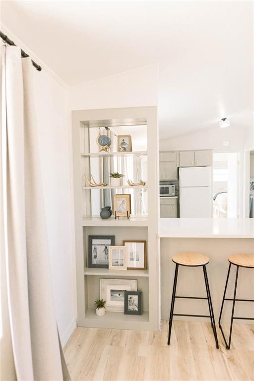 kitchen featuring white refrigerator, lofted ceiling, a kitchen bar, and light hardwood / wood-style flooring