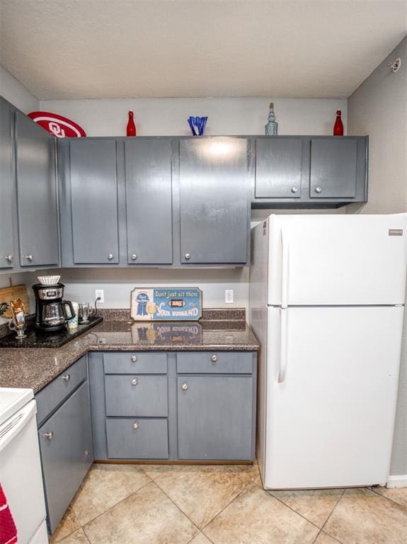 kitchen featuring gray cabinets, light tile patterned floors, white fridge, and dark stone countertops