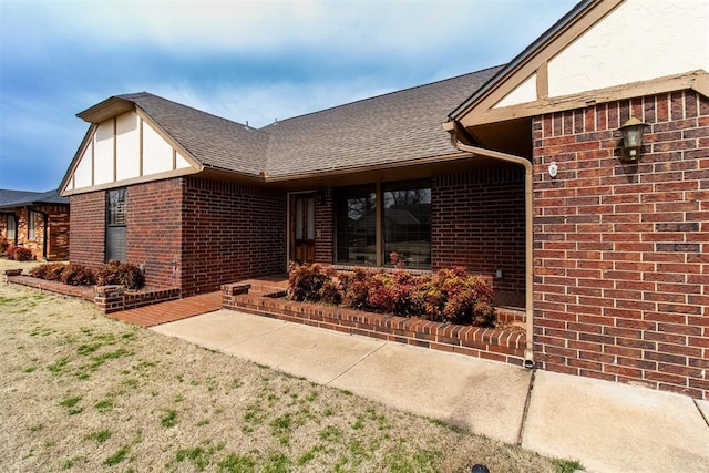 view of exterior entry featuring brick siding and a shingled roof