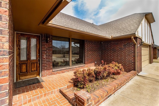 view of exterior entry featuring a garage, brick siding, and a shingled roof