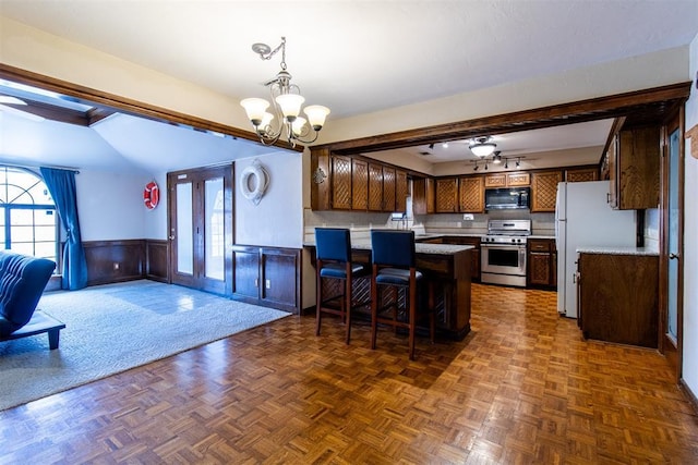 kitchen featuring open floor plan, freestanding refrigerator, black microwave, wainscoting, and stainless steel gas range