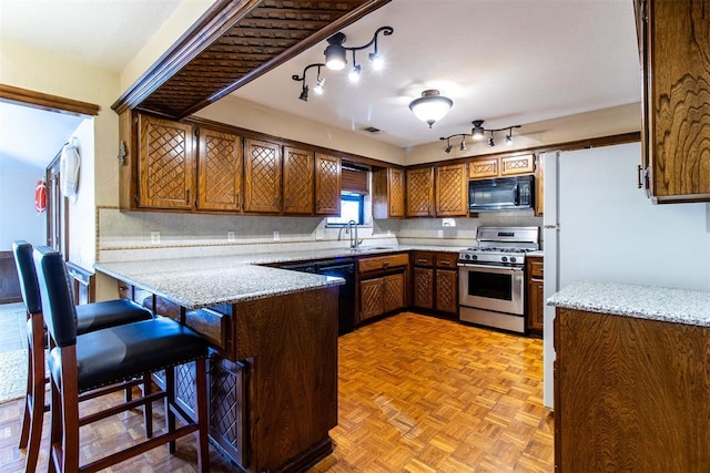 kitchen with tasteful backsplash, light stone countertops, a peninsula, brown cabinetry, and black appliances