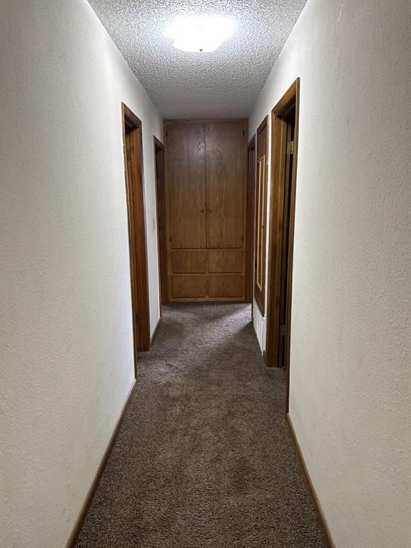 hallway featuring a textured ceiling and dark colored carpet