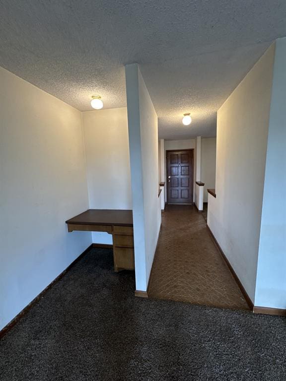 corridor with a textured ceiling and dark carpet