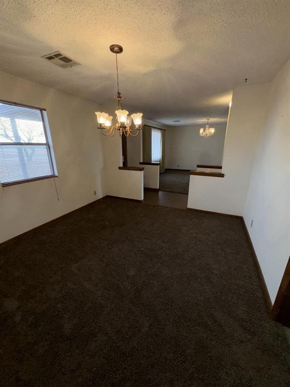 carpeted spare room with a notable chandelier and a textured ceiling