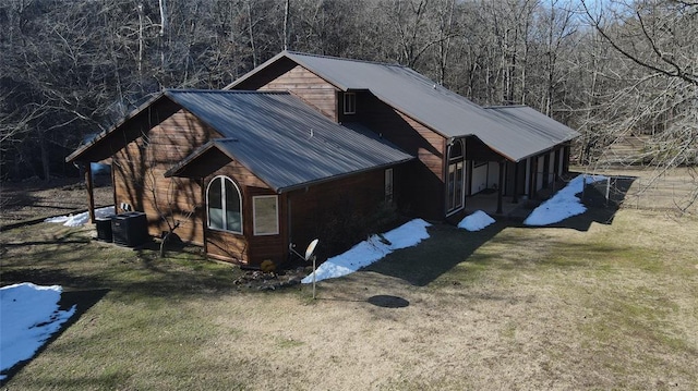 view of side of property with a forest view, a lawn, metal roof, and central AC