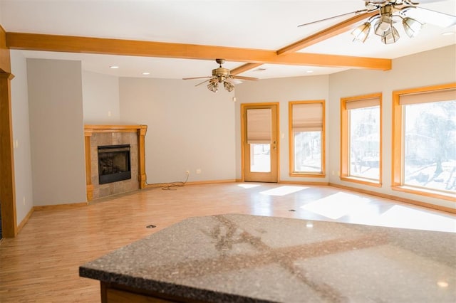 unfurnished living room featuring beam ceiling, a fireplace, light wood finished floors, baseboards, and ceiling fan