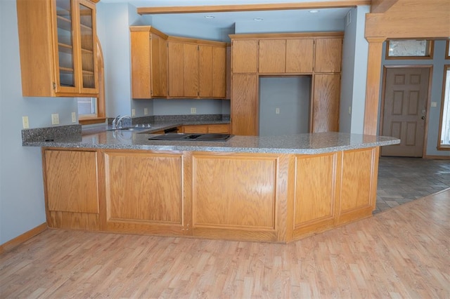 kitchen with sink, dark stone counters, kitchen peninsula, black electric stovetop, and light hardwood / wood-style floors