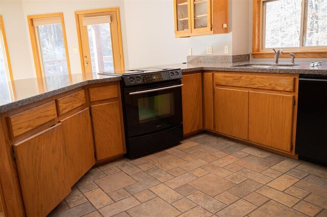 kitchen featuring glass insert cabinets, dark stone counters, stone tile flooring, black appliances, and a sink