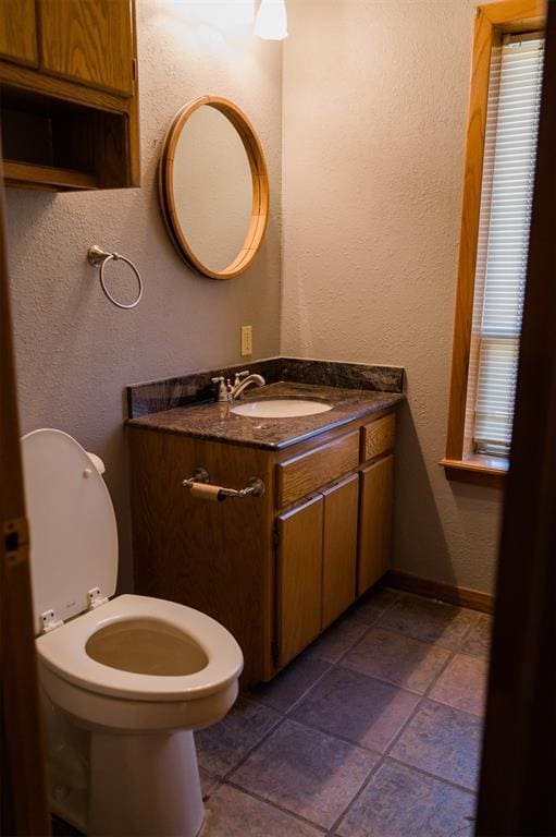 half bath featuring baseboards, toilet, vanity, and a textured wall