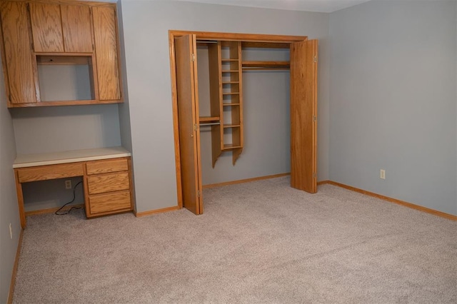 unfurnished bedroom featuring light carpet, built in desk, a closet, and baseboards