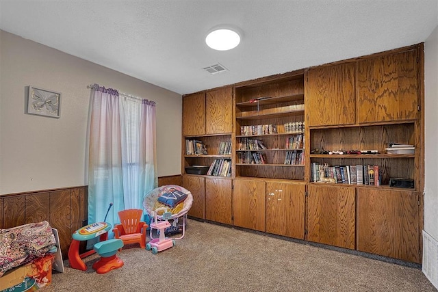 recreation room with a textured ceiling, light carpet, and wood walls