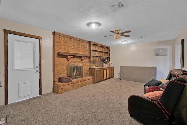 living room with ceiling fan, carpet flooring, a brick fireplace, and a textured ceiling