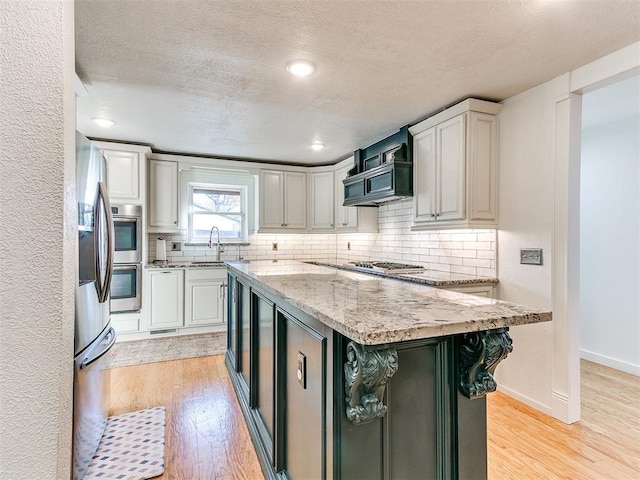 kitchen featuring sink, a center island, a textured ceiling, light wood-type flooring, and light stone countertops