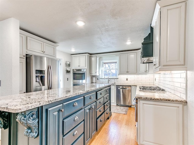 kitchen featuring light hardwood / wood-style flooring, blue cabinetry, appliances with stainless steel finishes, tasteful backsplash, and white cabinets