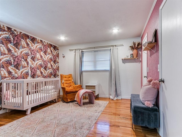 bedroom featuring a nursery area, wood-type flooring, and crown molding