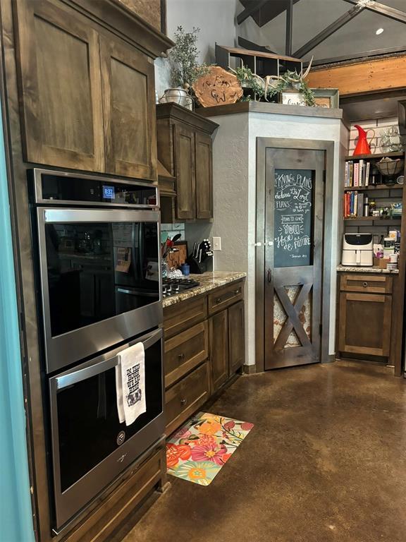 kitchen featuring stainless steel double oven, light stone counters, dark brown cabinetry, and wall chimney exhaust hood