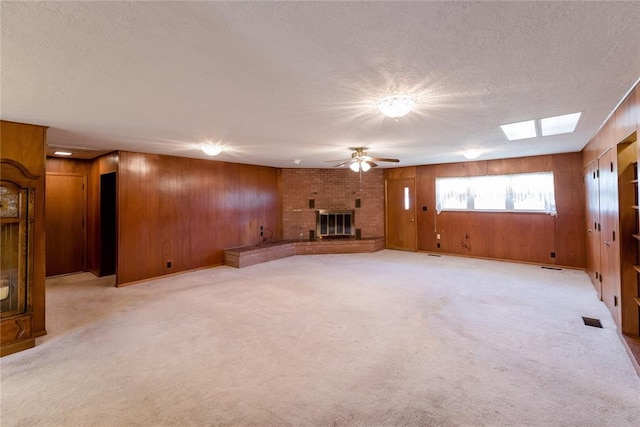 unfurnished living room featuring a brick fireplace, light colored carpet, a textured ceiling, and wooden walls