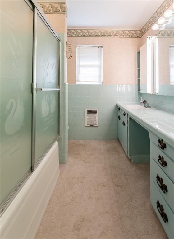 bathroom featuring tile walls, vanity, heating unit, and enclosed tub / shower combo