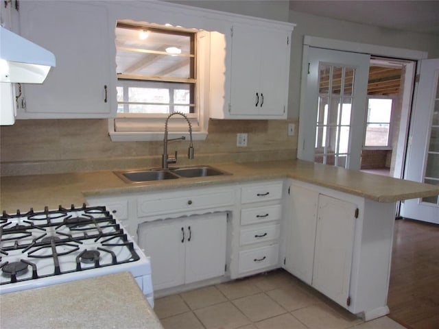 kitchen with tasteful backsplash, white cabinetry, white gas range, and sink