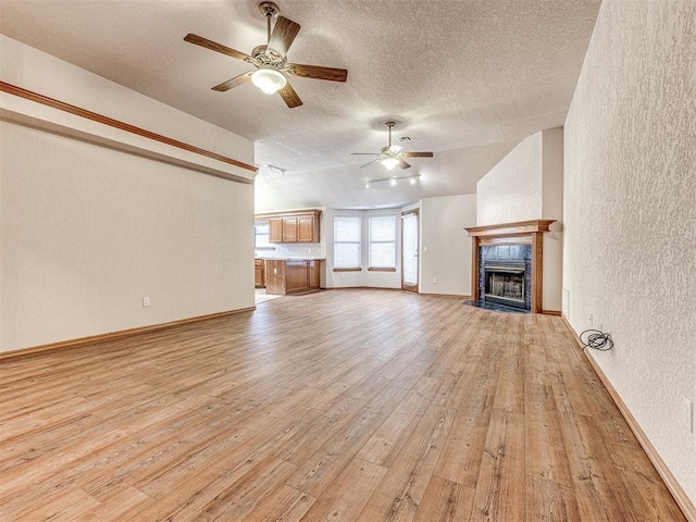 unfurnished living room featuring ceiling fan, a textured ceiling, a tiled fireplace, vaulted ceiling, and light wood-type flooring