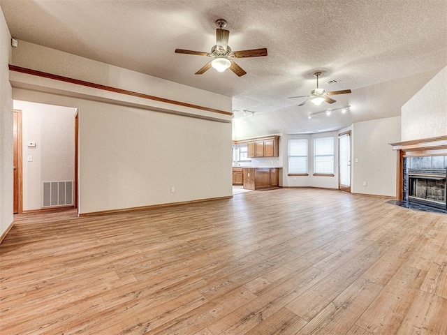 unfurnished living room featuring a tile fireplace, ceiling fan, light hardwood / wood-style floors, a textured ceiling, and vaulted ceiling