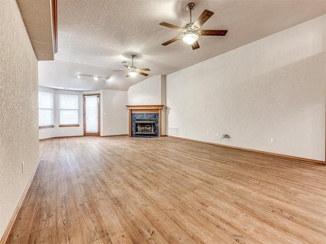 unfurnished living room featuring vaulted ceiling, a textured ceiling, light wood-type flooring, ceiling fan, and a tiled fireplace