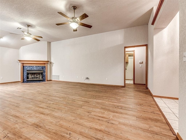 unfurnished living room with lofted ceiling, light wood-type flooring, ceiling fan, a premium fireplace, and a textured ceiling