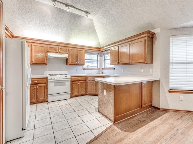 kitchen with lofted ceiling, sink, white appliances, a textured ceiling, and kitchen peninsula