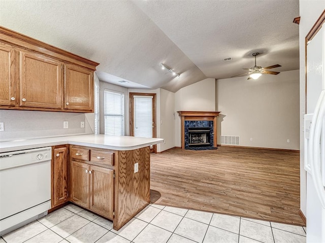 kitchen with lofted ceiling, light tile patterned floors, kitchen peninsula, white appliances, and a high end fireplace