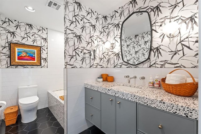 bathroom featuring tile patterned floors, toilet, tile walls, vanity, and a bathing tub