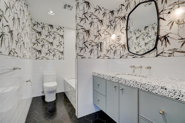 bathroom featuring tile walls, vanity, a washtub, toilet, and tile patterned floors