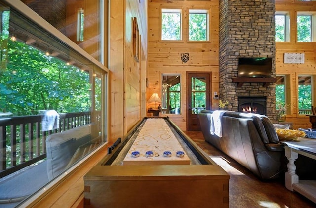 game room featuring a high ceiling, a stone fireplace, and wooden walls