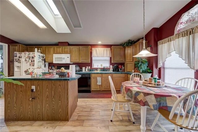 kitchen featuring lofted ceiling with skylight, sink, light wood-type flooring, pendant lighting, and white appliances