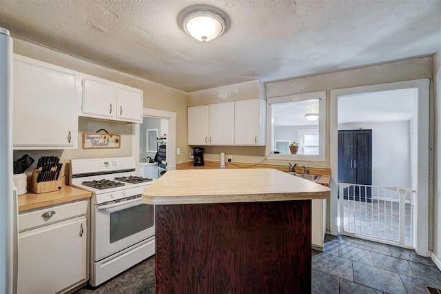 kitchen featuring white cabinetry, white gas range, a center island, and a textured ceiling