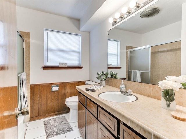 bathroom featuring tile patterned floors, toilet, a shower with shower door, wood walls, and vanity