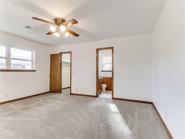 unfurnished bedroom with a walk in closet, connected bathroom, light carpet, and ceiling fan