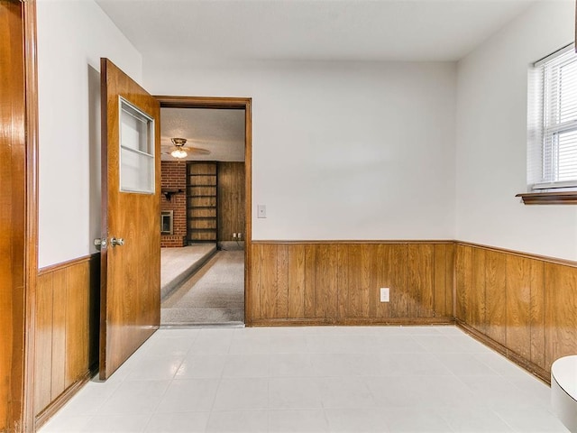 unfurnished room featuring ceiling fan, wooden walls, and a brick fireplace