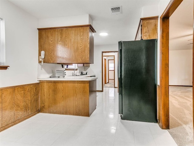 kitchen featuring sink, light tile patterned floors, black refrigerator, wooden walls, and kitchen peninsula