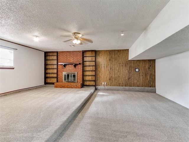 unfurnished living room with wood walls, light colored carpet, ceiling fan, a brick fireplace, and a textured ceiling