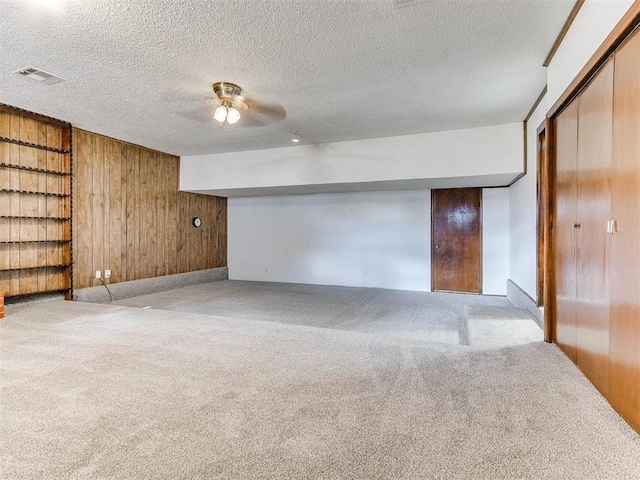 interior space featuring light colored carpet, a textured ceiling, and wood walls