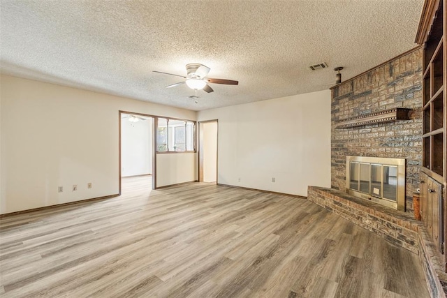 unfurnished living room featuring ceiling fan, a textured ceiling, a fireplace, and light wood-type flooring