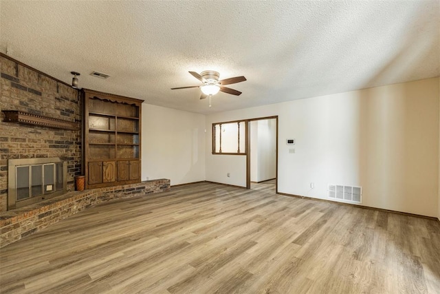 unfurnished living room featuring ceiling fan, a brick fireplace, a textured ceiling, and light hardwood / wood-style flooring