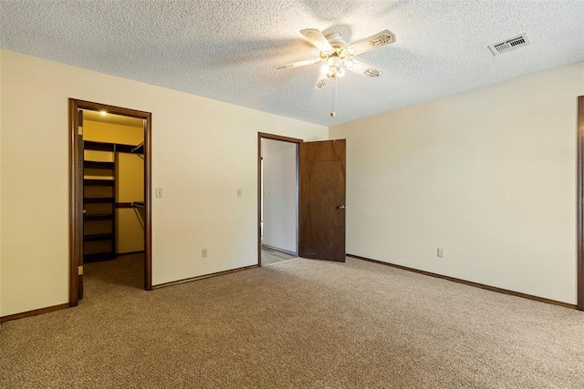 unfurnished bedroom with a walk in closet, light colored carpet, a textured ceiling, a closet, and ceiling fan