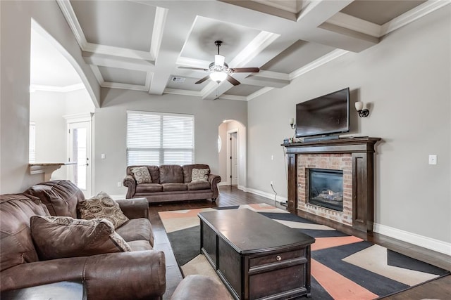 living room with a brick fireplace, beam ceiling, and light hardwood / wood-style flooring